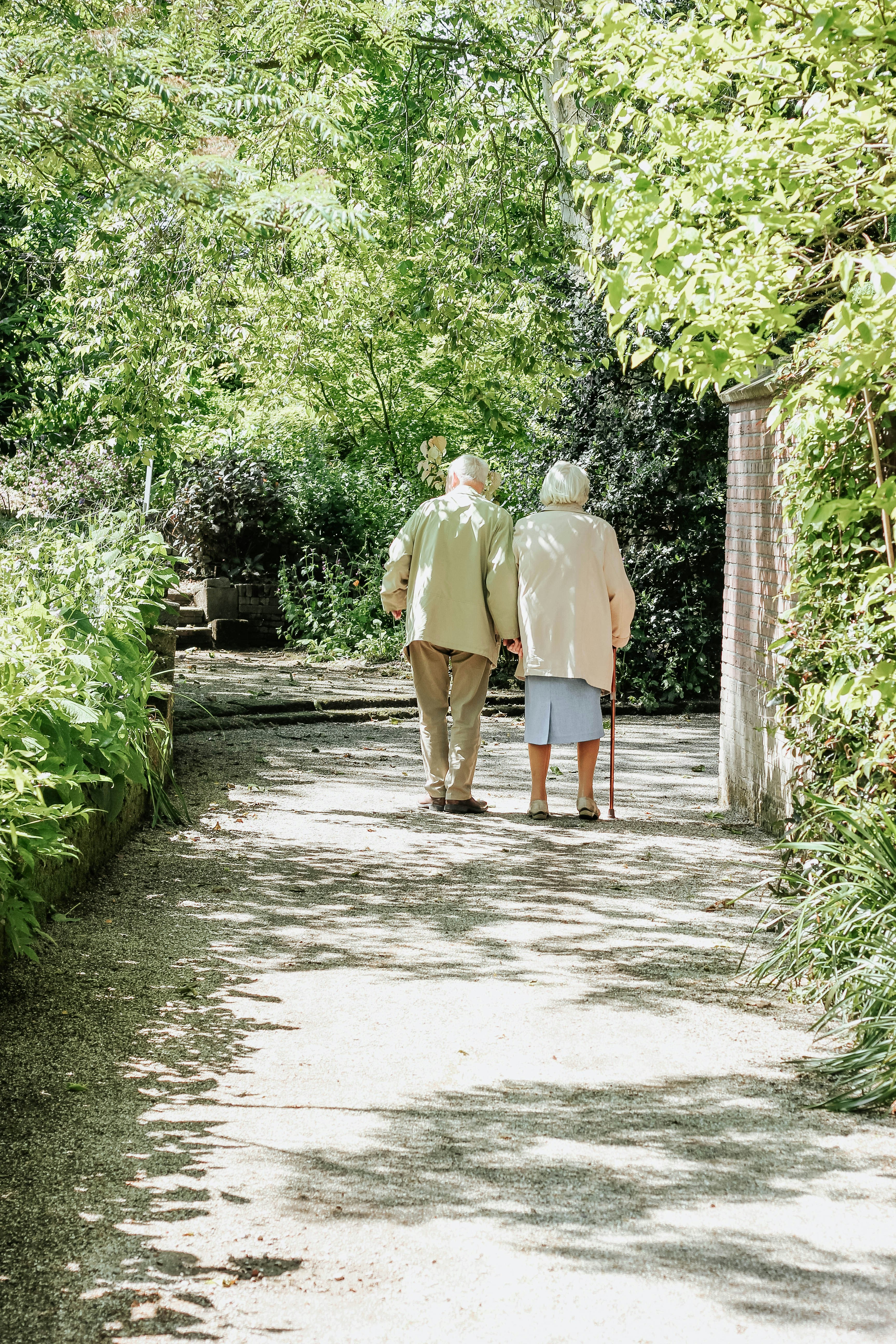 Senior couple walking a path under the trees in the sun.